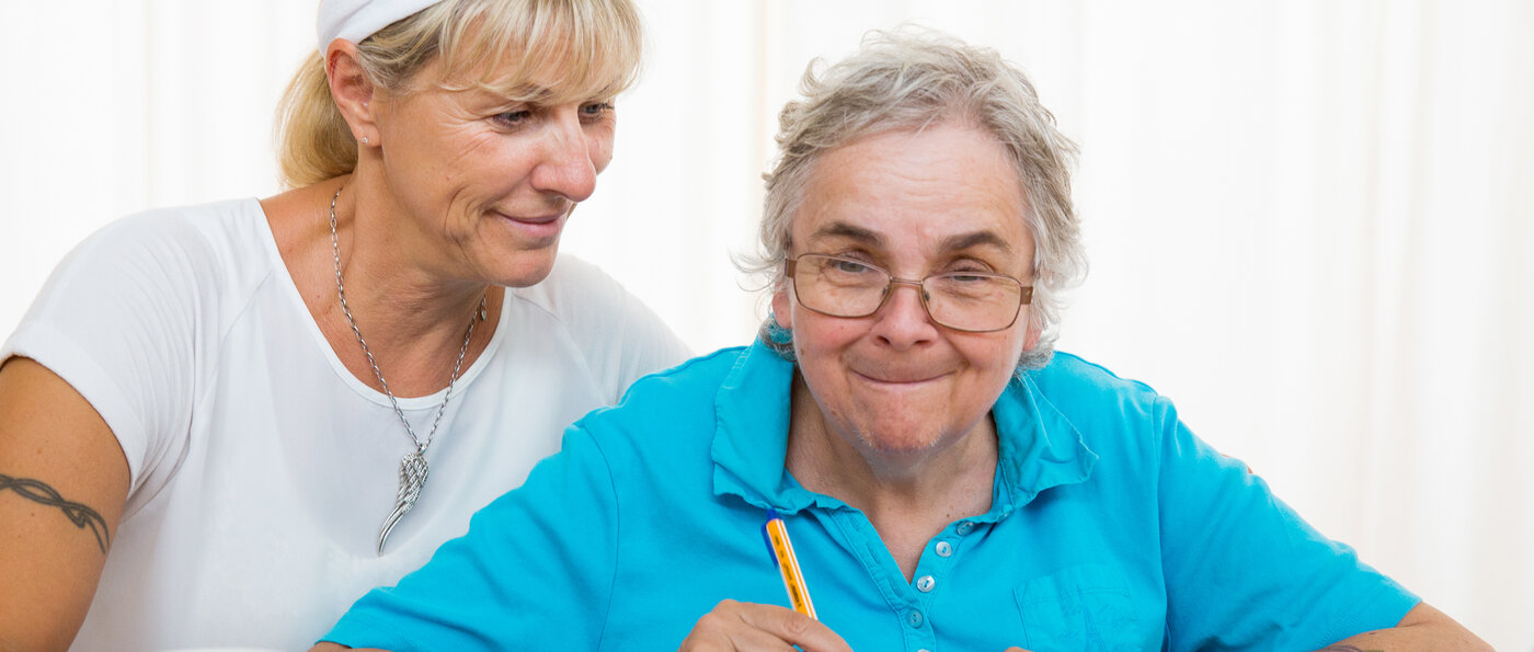 Eine Betreuerin hilft einer alten Dame beim Kreuzworträtsel lösen