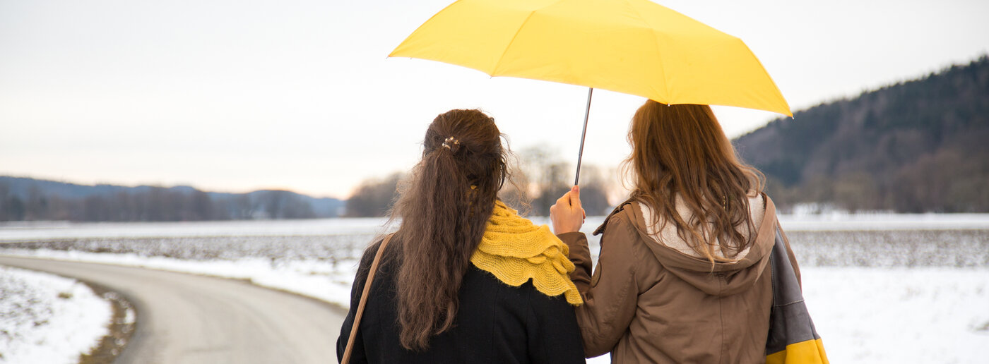 Zwei junge Frauen gehen mit gelbem Regenschirm auf einem Weg.