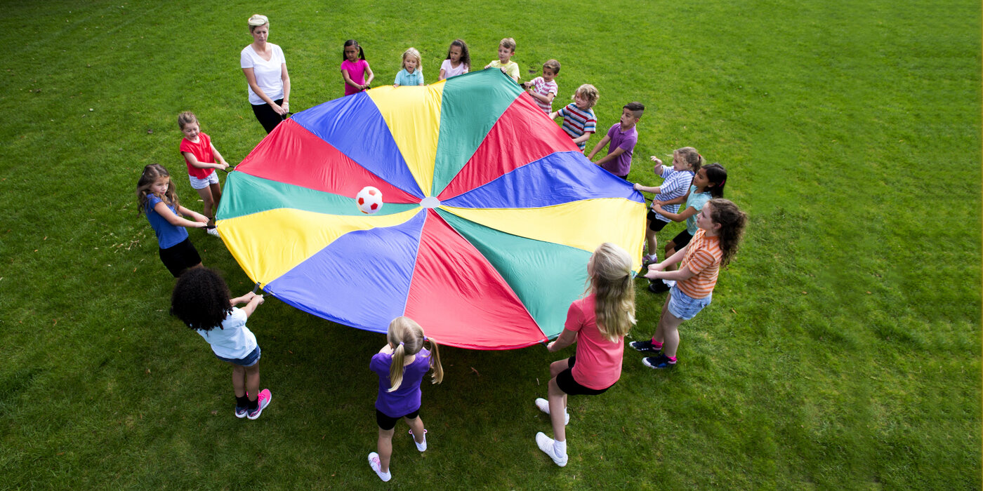 Freizeitbetreuung: Kinder spielen mit dem Schwungtuch und Ball.