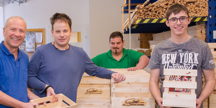 Vier Leute arbeiten in einer Holzwerkstatt und in der Hand halten sie eine Holzkiste.